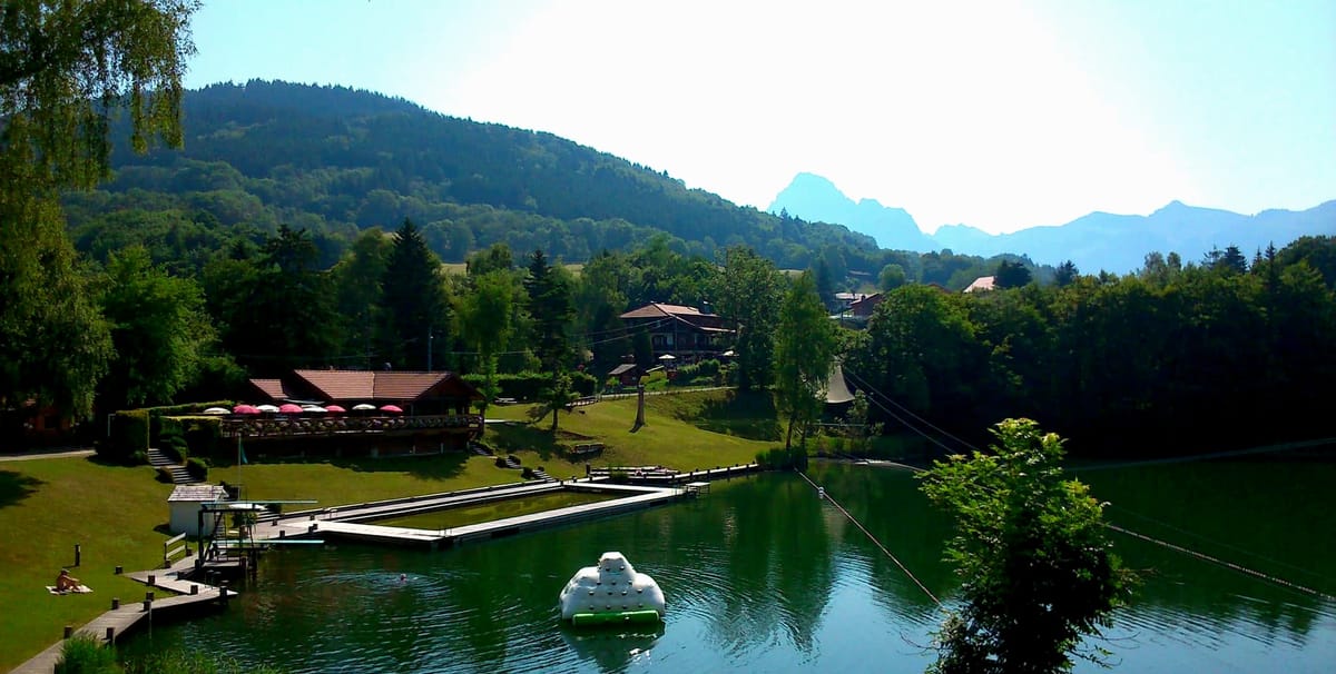 Vue panoramique sur la plage du lac de la Beunaz en été : le restaurant À la Belle Étoile, le ponton et les montagnes du Chablais