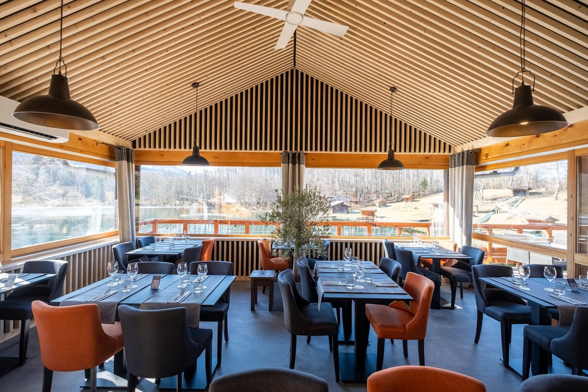 Salle du restaurant sous charpente bois, ouverte sur le lac